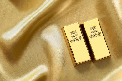 Photo of Gold bars on shiny silk fabric, flat lay. Space for text