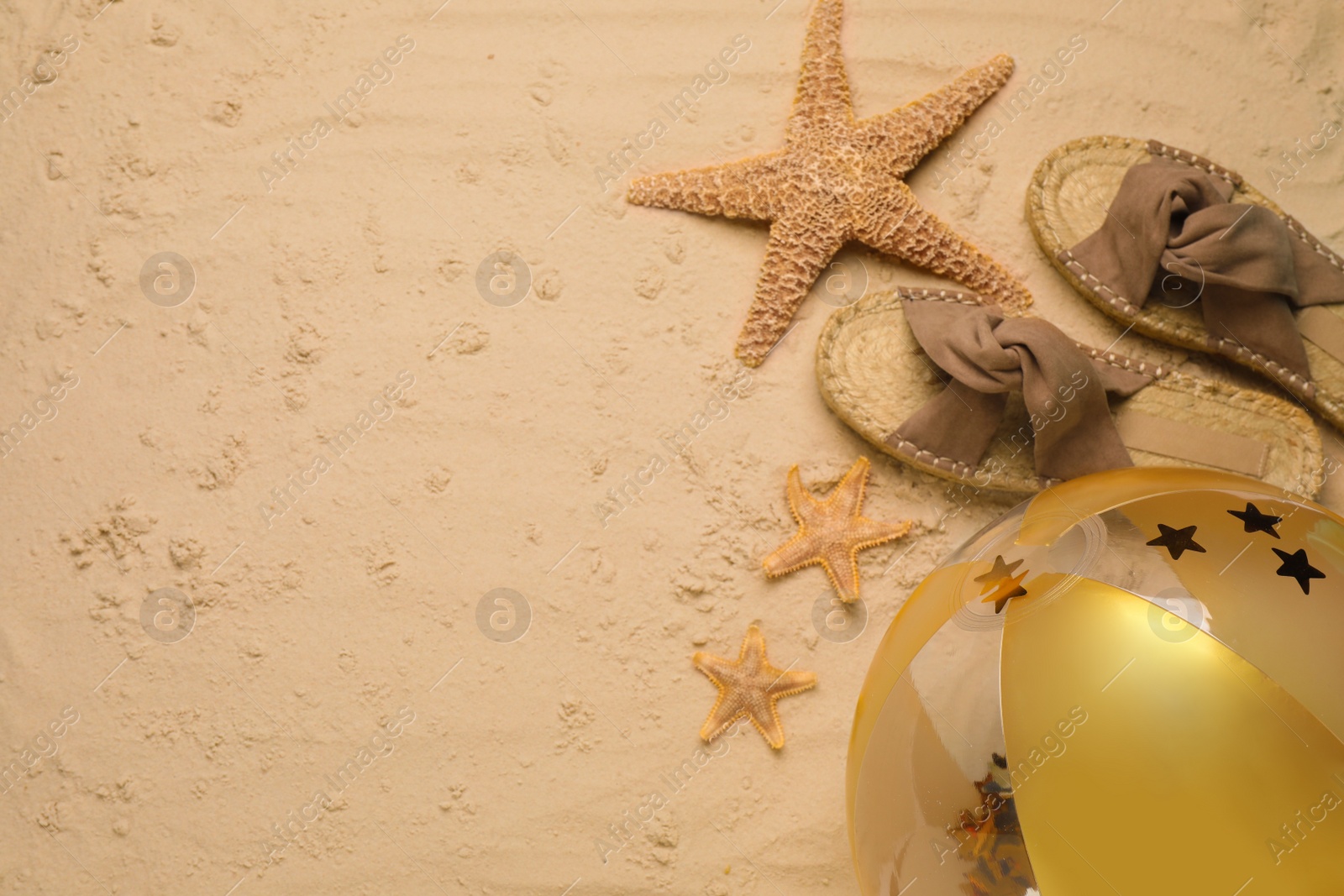 Photo of Beach ball, slippers and starfishes on sand, flat lay. Space for text