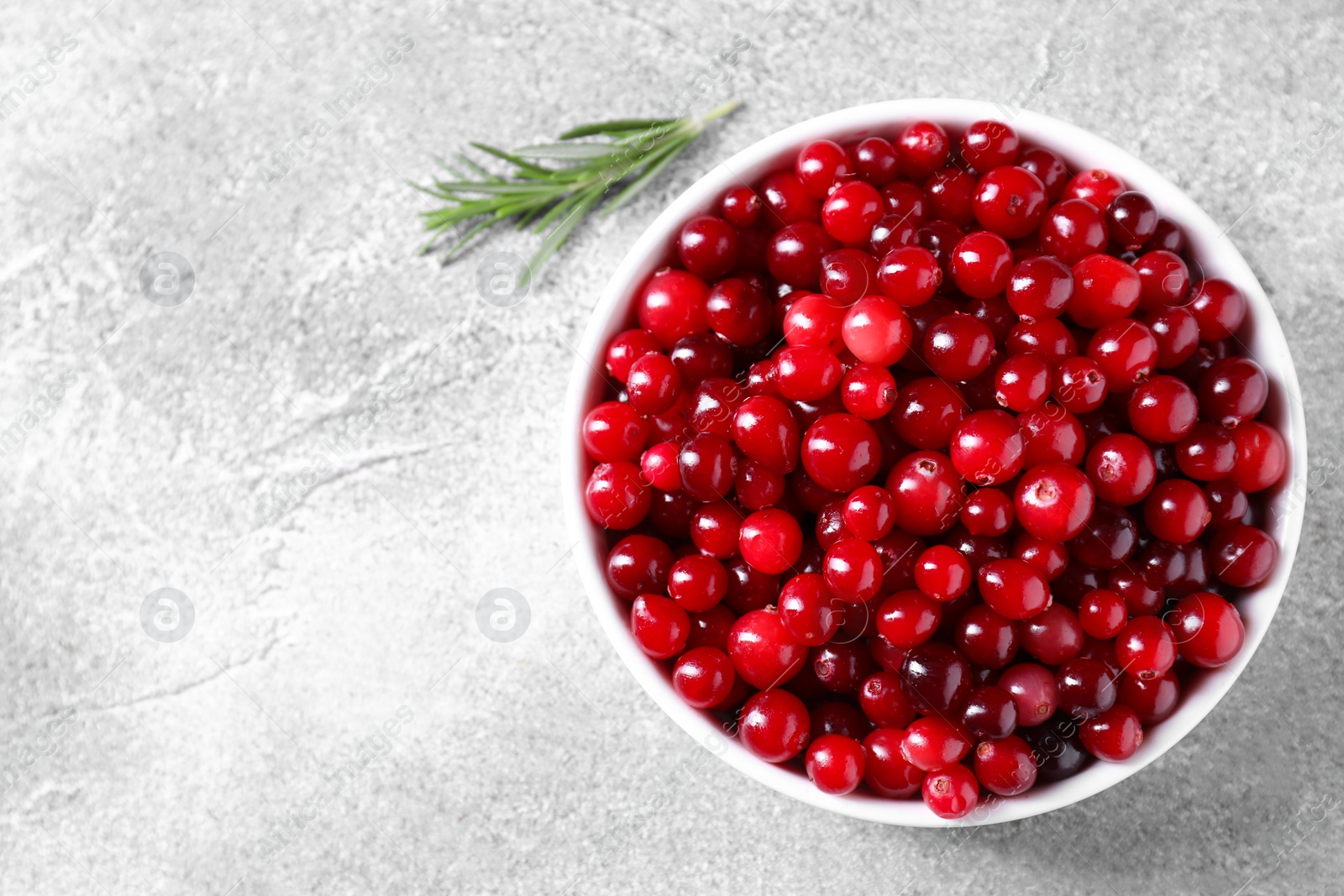 Photo of Fresh ripe cranberries in bowl on grey table, top view. Space for text