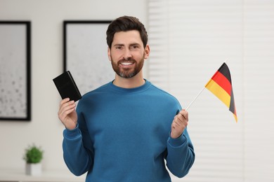 Photo of Immigration. Happy man with passport and flag of Germany indoors