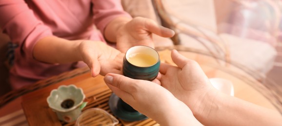Image of Woman giving cup with drink above table, closeup. Tea ceremony