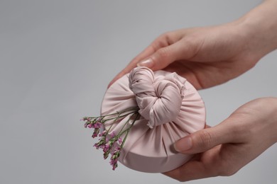 Photo of Furoshiki technique. Woman holding gift packed in fabric and beautiful pink flowers on gray background, closeup with space for text