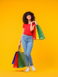 Happy young woman with shopping bags on yellow background. Space for text