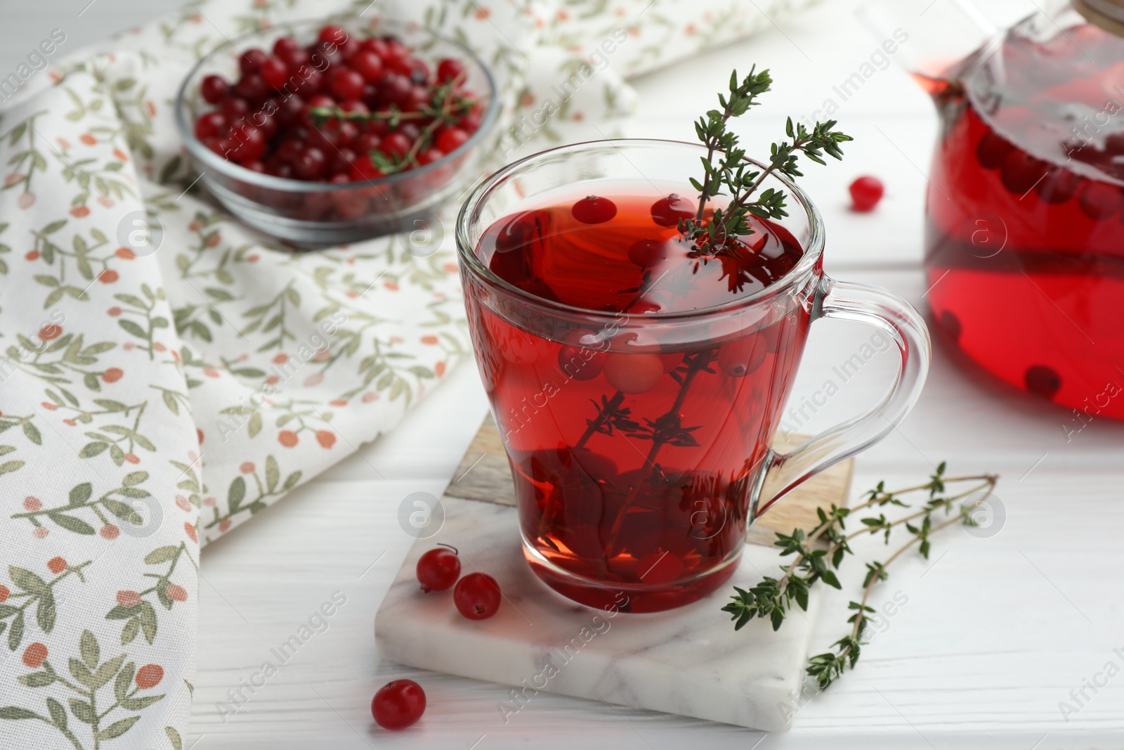 Photo of Tasty hot cranberry tea with thyme and fresh berries in glass cup on white wooden table