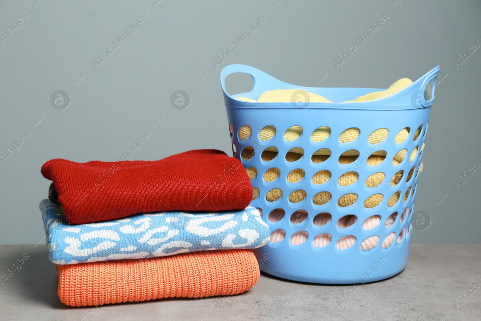 Photo of Plastic laundry basket and clean clothes on grey table