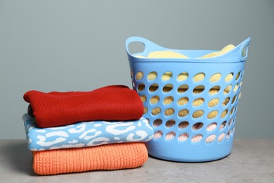Photo of Plastic laundry basket and clean clothes on grey table