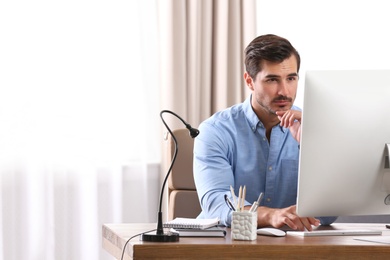 Handsome young man working with computer at table in office