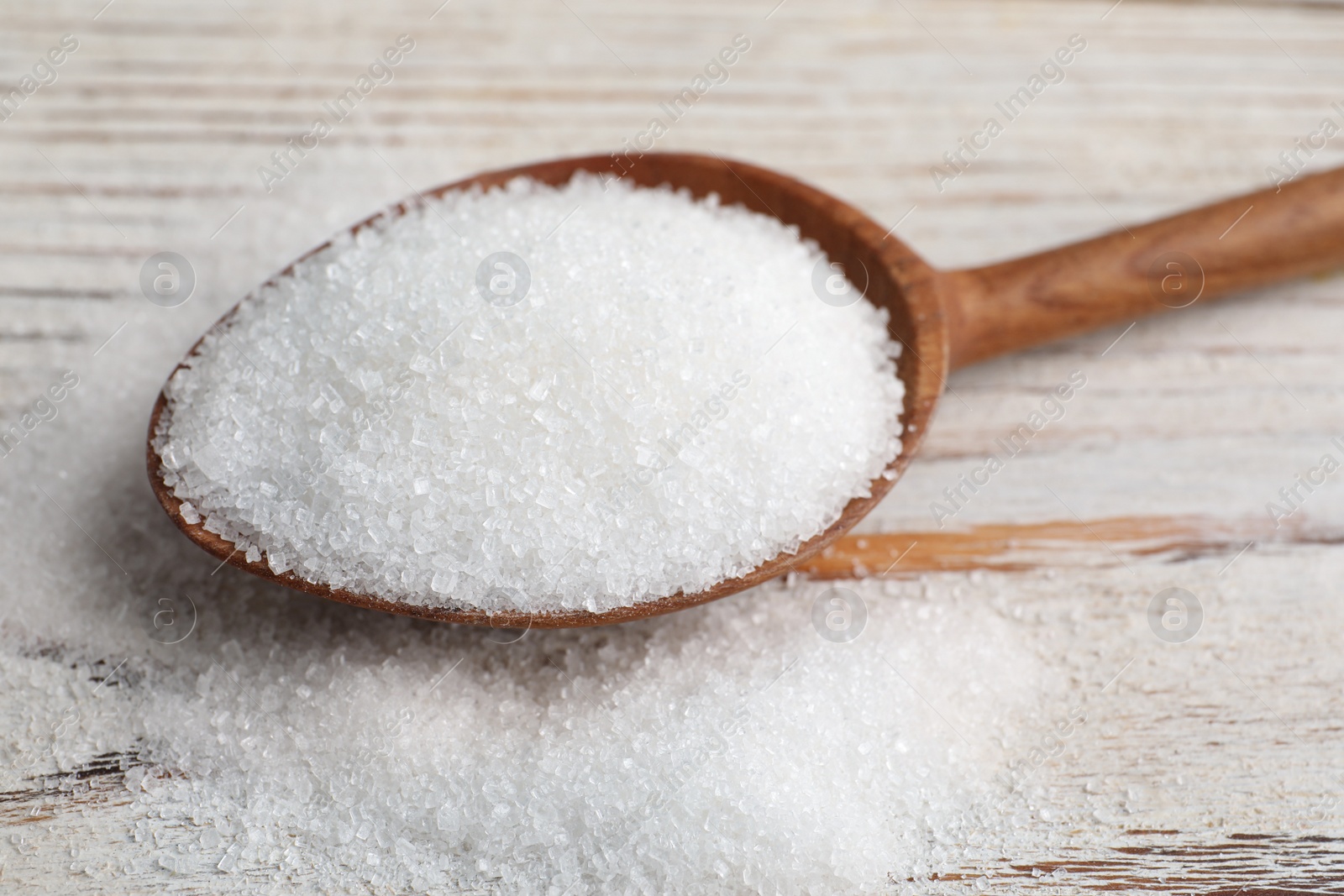 Photo of Spoon with granulated sugar on white wooden table, closeup