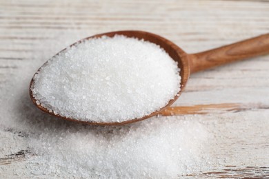 Photo of Spoon with granulated sugar on white wooden table, closeup