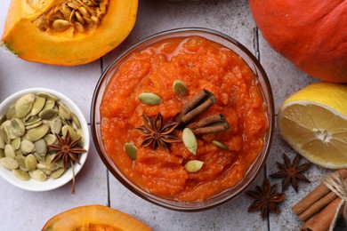 Photo of Bowl of delicious pumpkin jam and ingredients on tiled surface, flat lay