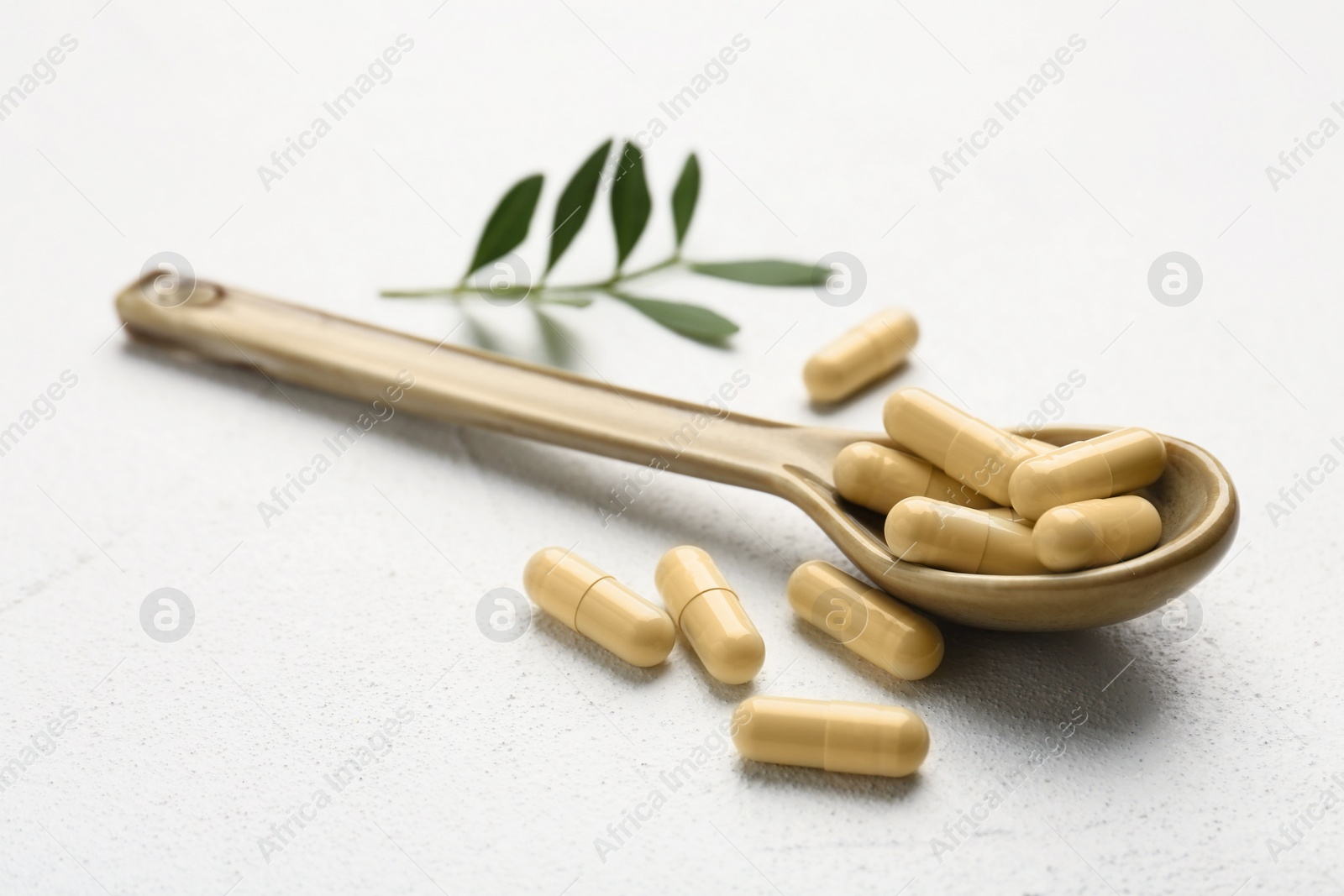 Photo of Vitamin capsules in spoon and leaves on white wooden table, closeup