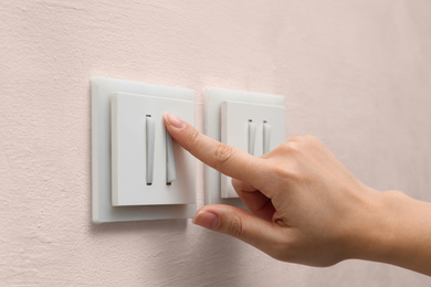 Photo of Woman pressing button of light switch indoors, closeup