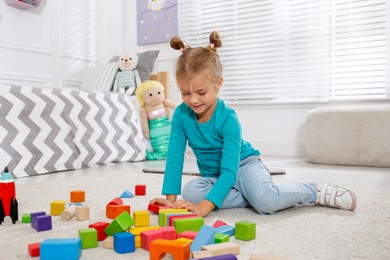 Cute little girl playing with colorful building blocks at home
