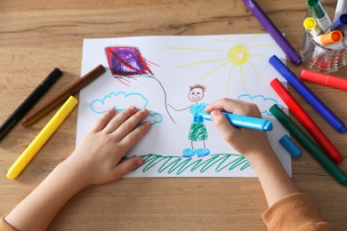 Little girl drawing picture with marker at wooden table, top view. Child`s art