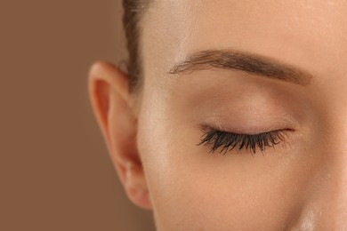 Photo of Woman with long eyelashes after mascara applying against light brown background, closeup