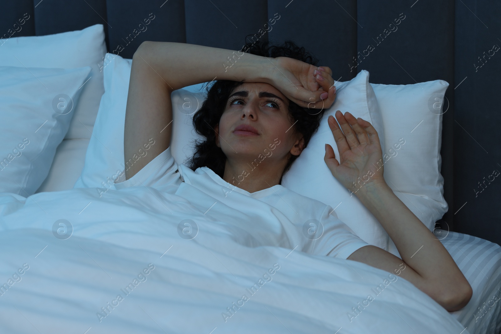 Photo of Young woman suffering from headache in bed at night