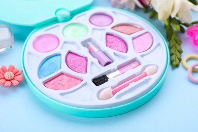 Photo of Decorative cosmetics for kids. Eye shadow palette, accessories and flowers on light blue background, closeup
