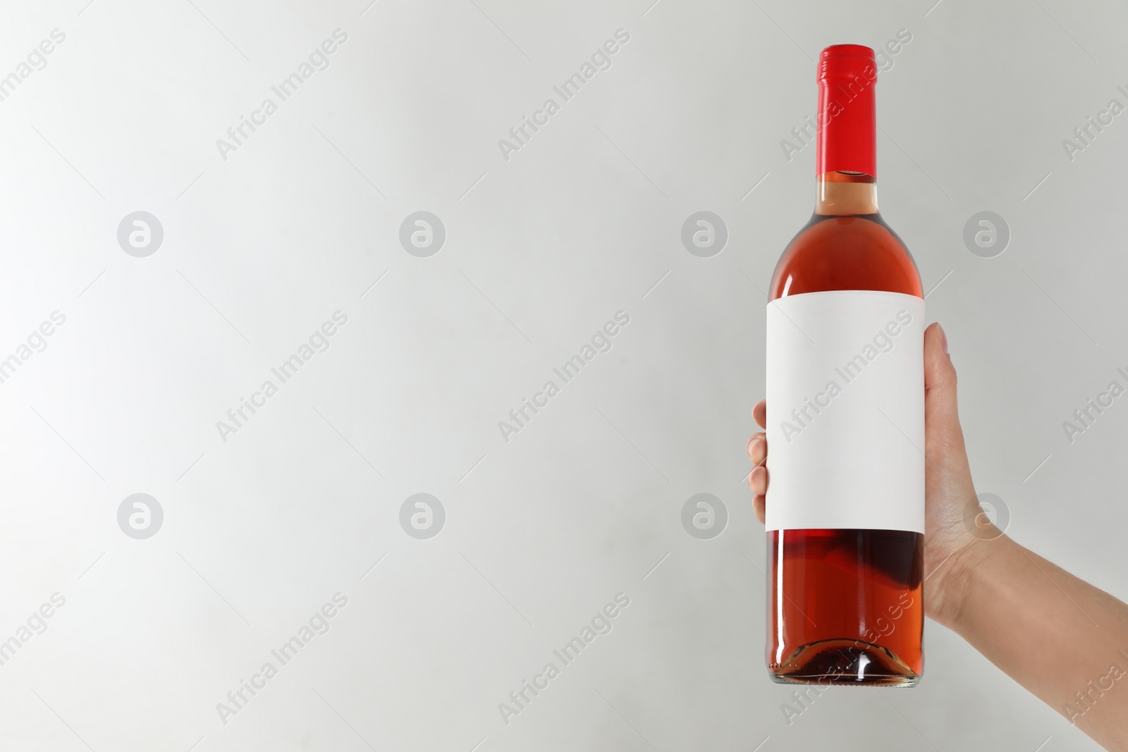 Photo of Woman holding bottle of rose wine on light background, closeup. Space for text