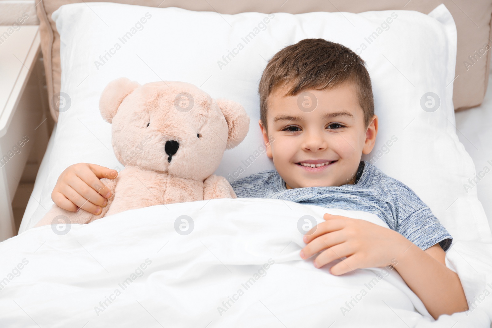 Photo of Cute child with teddy bear resting in bed at hospital