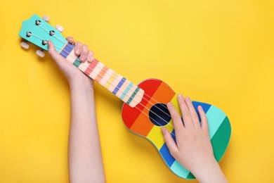 Photo of Woman holding ukulele on yellow background, closeup. String musical instrument