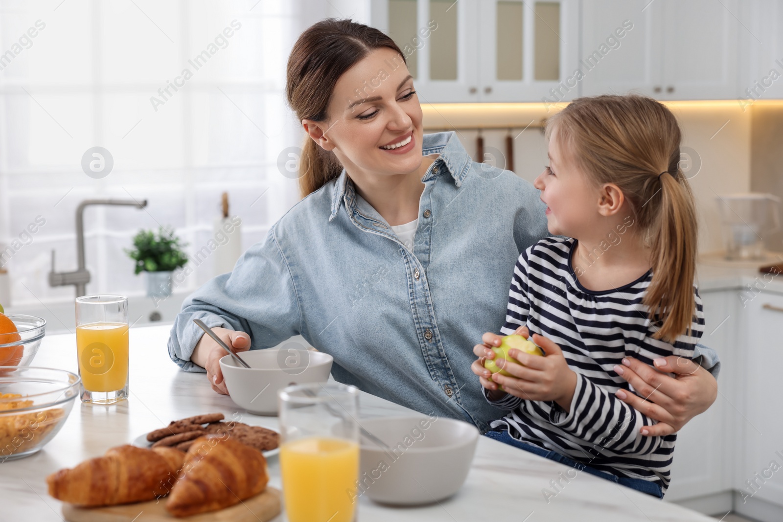 Photo of Mother and her cute little daughter having breakfast at table in kitchen