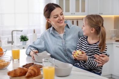 Mother and her cute little daughter having breakfast at table in kitchen