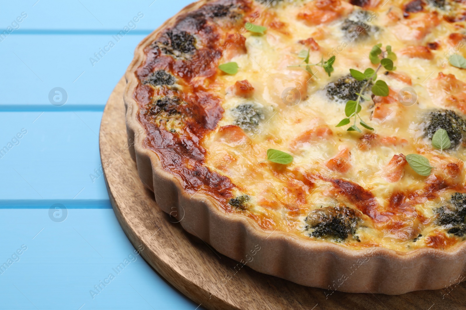 Photo of Delicious homemade quiche with salmon and broccoli on light blue wooden table, closeup