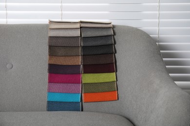 Photo of Catalog of colorful fabric samples on grey sofa indoors