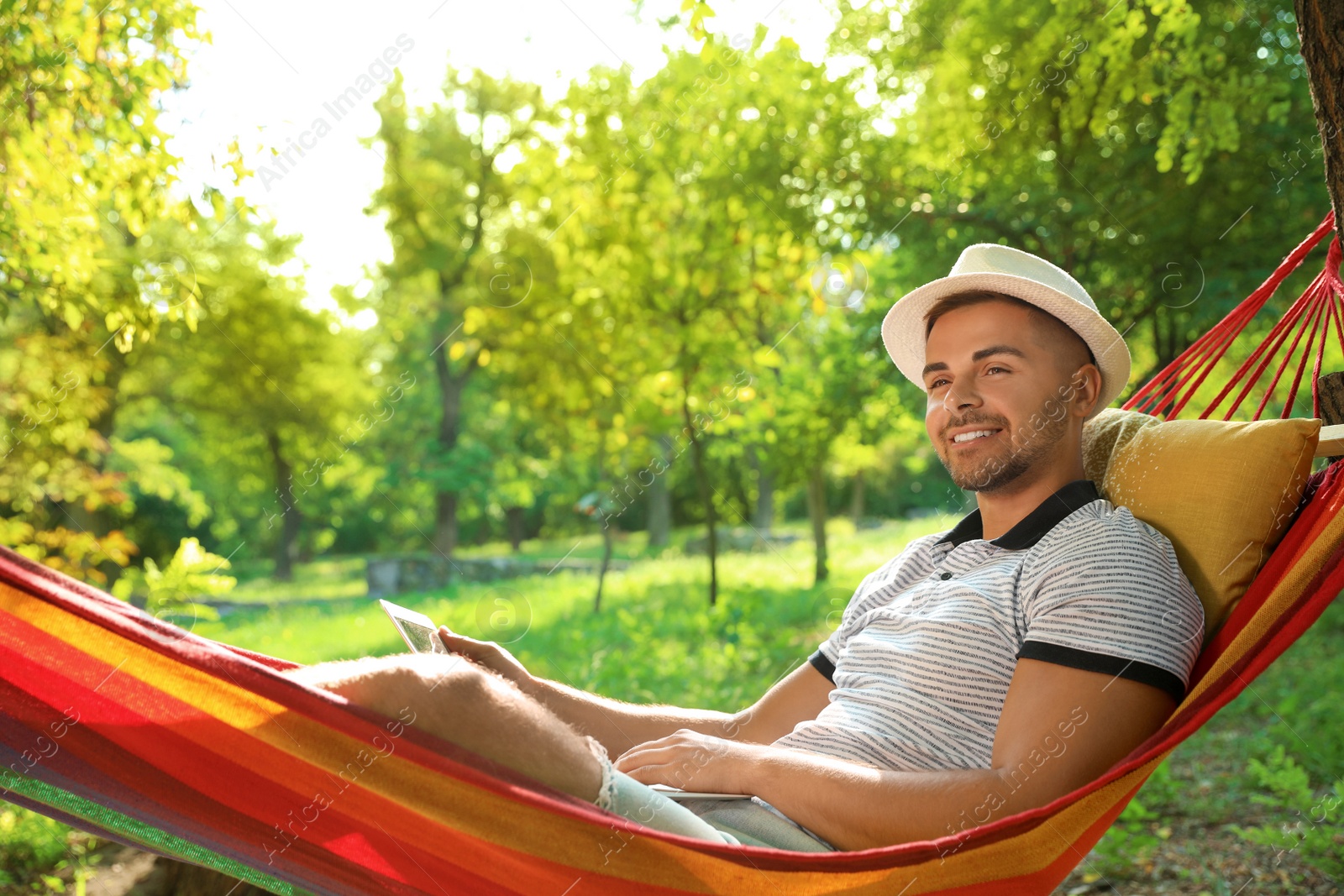 Photo of Young man with laptop resting in comfortable hammock at green garden