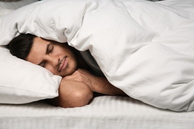 Handsome man sleeping under soft blanket in bed at home