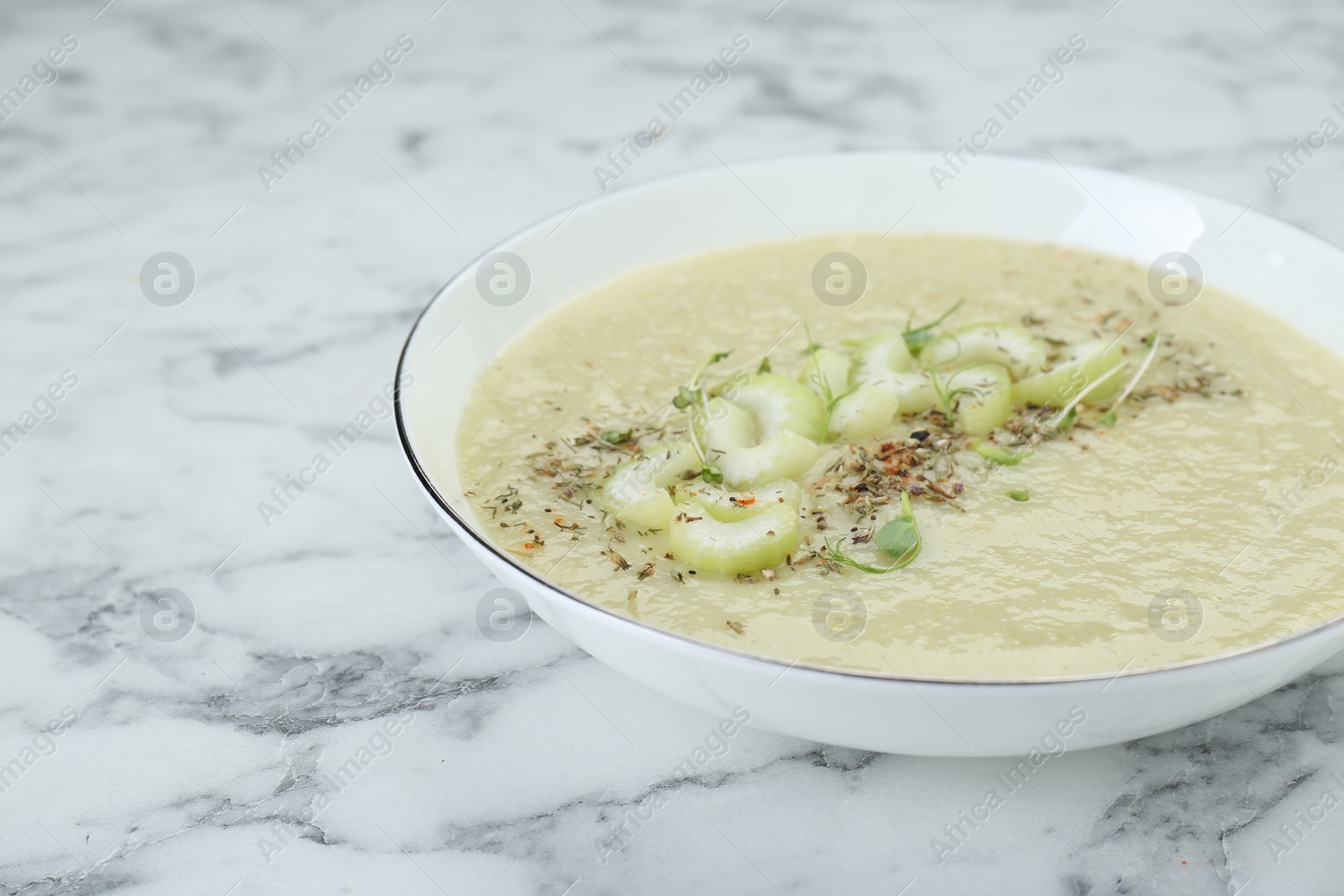 Photo of Bowl of delicious celery soup on white marble table, closeup