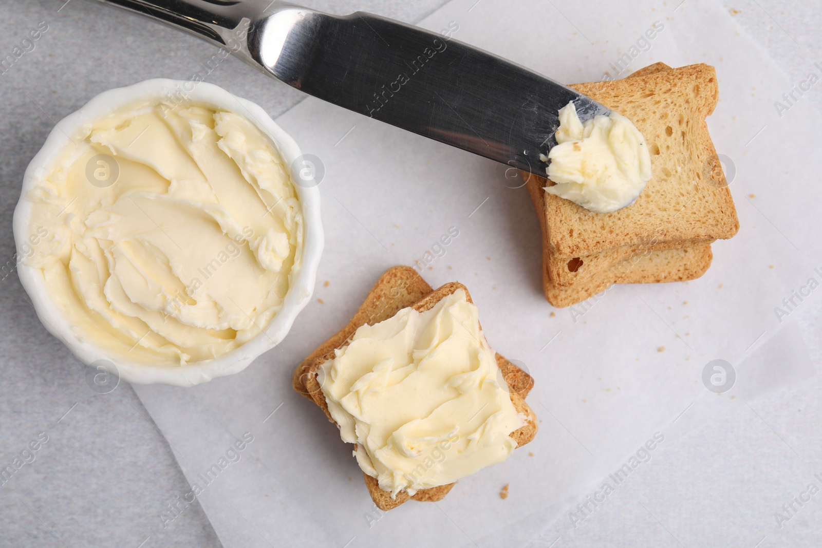 Photo of Slices of bread with tasty butter and knife on light gray table, flat lay