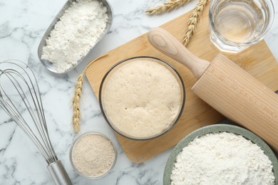 Leaven, flour, ears of wheat, rolling pin, whisk and water on white marble table, flat lay