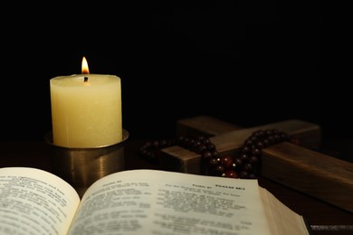 Photo of Church candle, Bible, wooden cross and rosary beads on table
