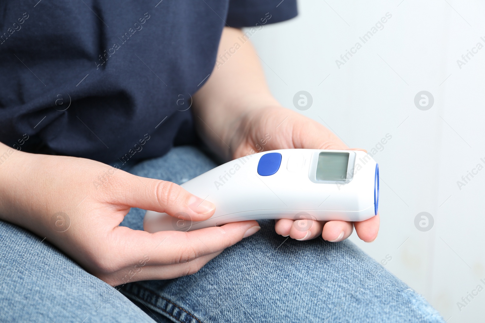 Photo of Woman with non contact infrared thermometer on light background, closeup