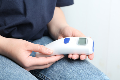 Photo of Woman with non contact infrared thermometer on light background, closeup