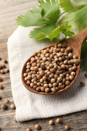 Photo of Spoon with dried coriander seeds and green leaves on wooden table, closeup