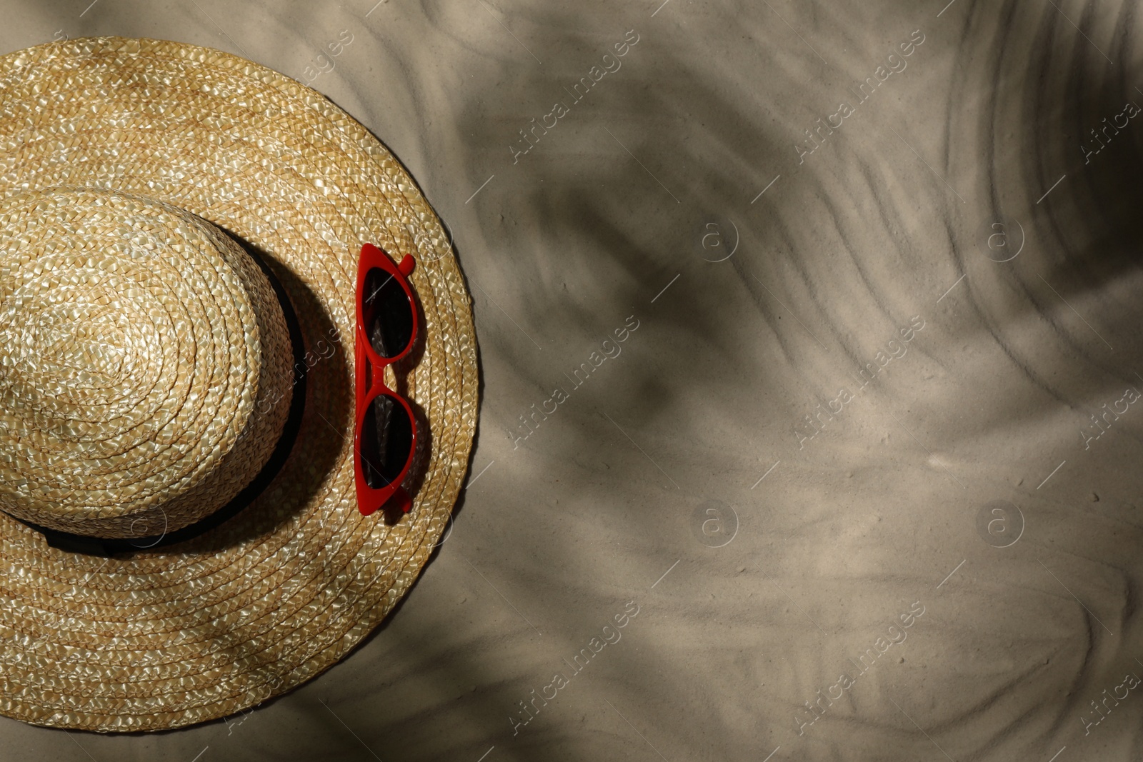 Photo of Straw hat and sunglasses on sand, top view. Beach accessories