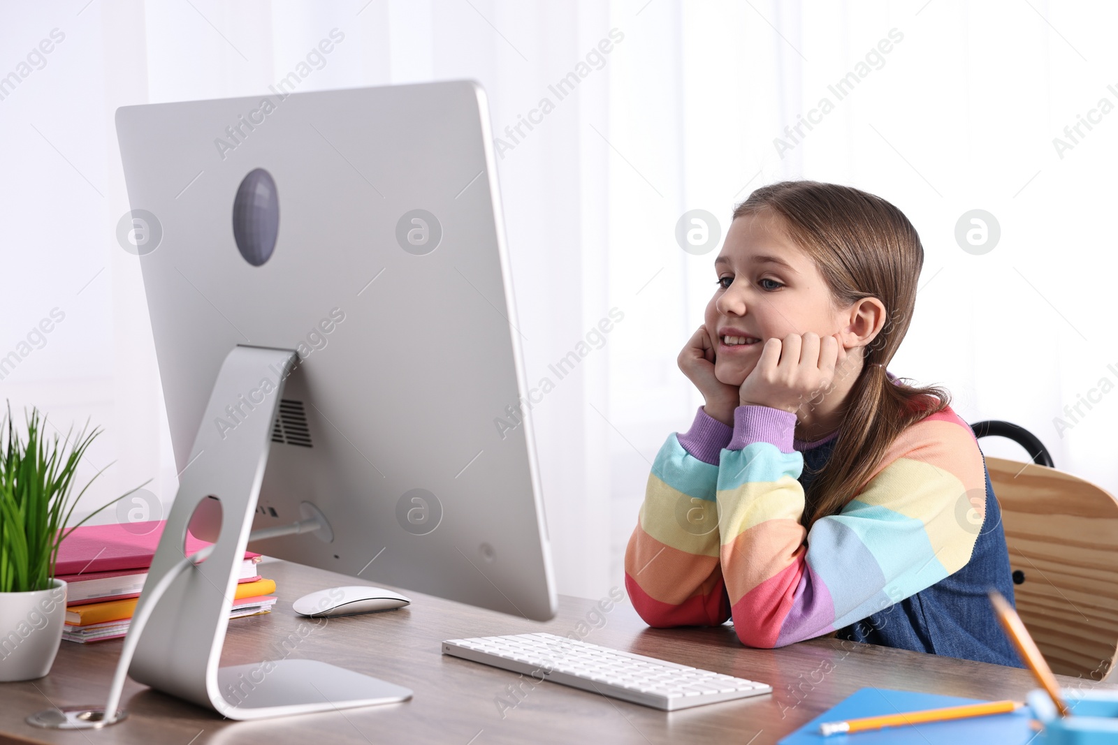 Photo of E-learning. Cute girl using computer during online lesson at table indoors