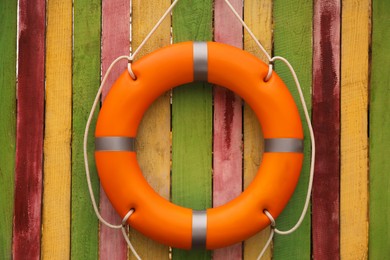 Photo of Orange lifebuoy hanging on color wooden fence. Rescue equipment