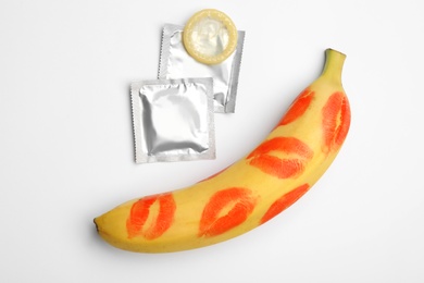 Photo of Condoms and banana with lipstick kiss marks on white background, top view. Safe sex