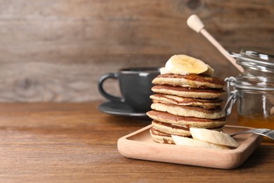 Photo of Plate of banana pancakes served on wooden table. Space for text