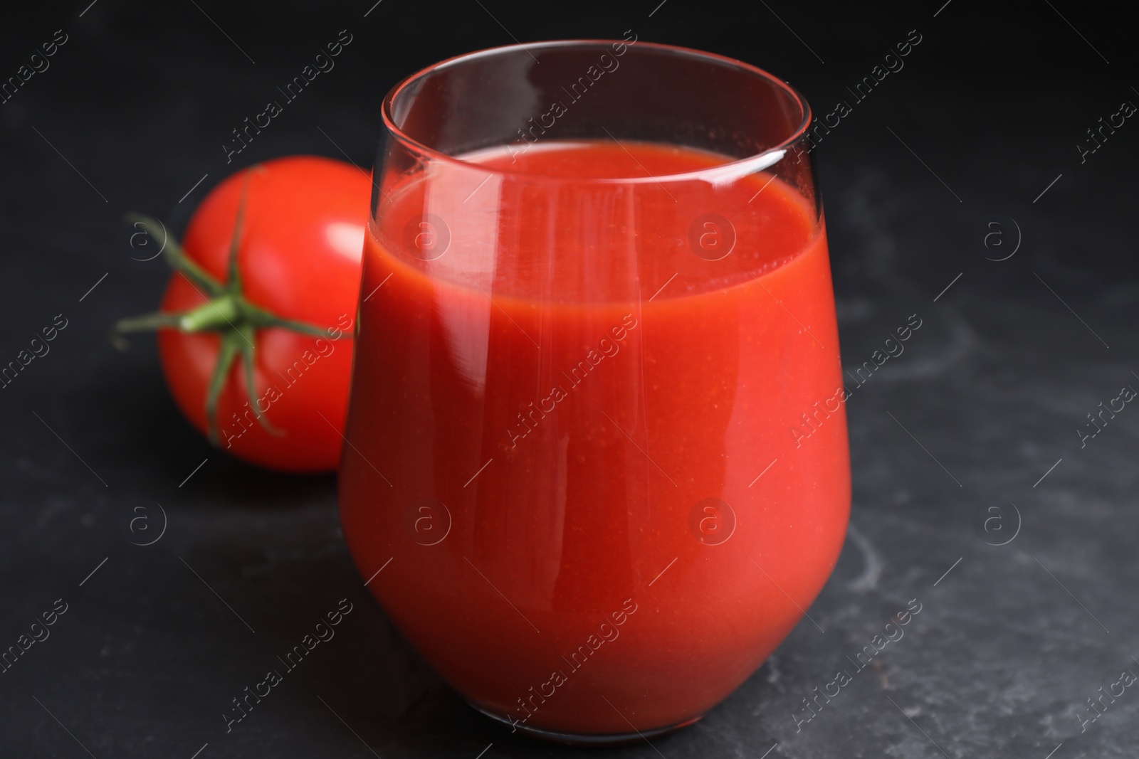 Photo of Delicious fresh tomato juice on black table, closeup