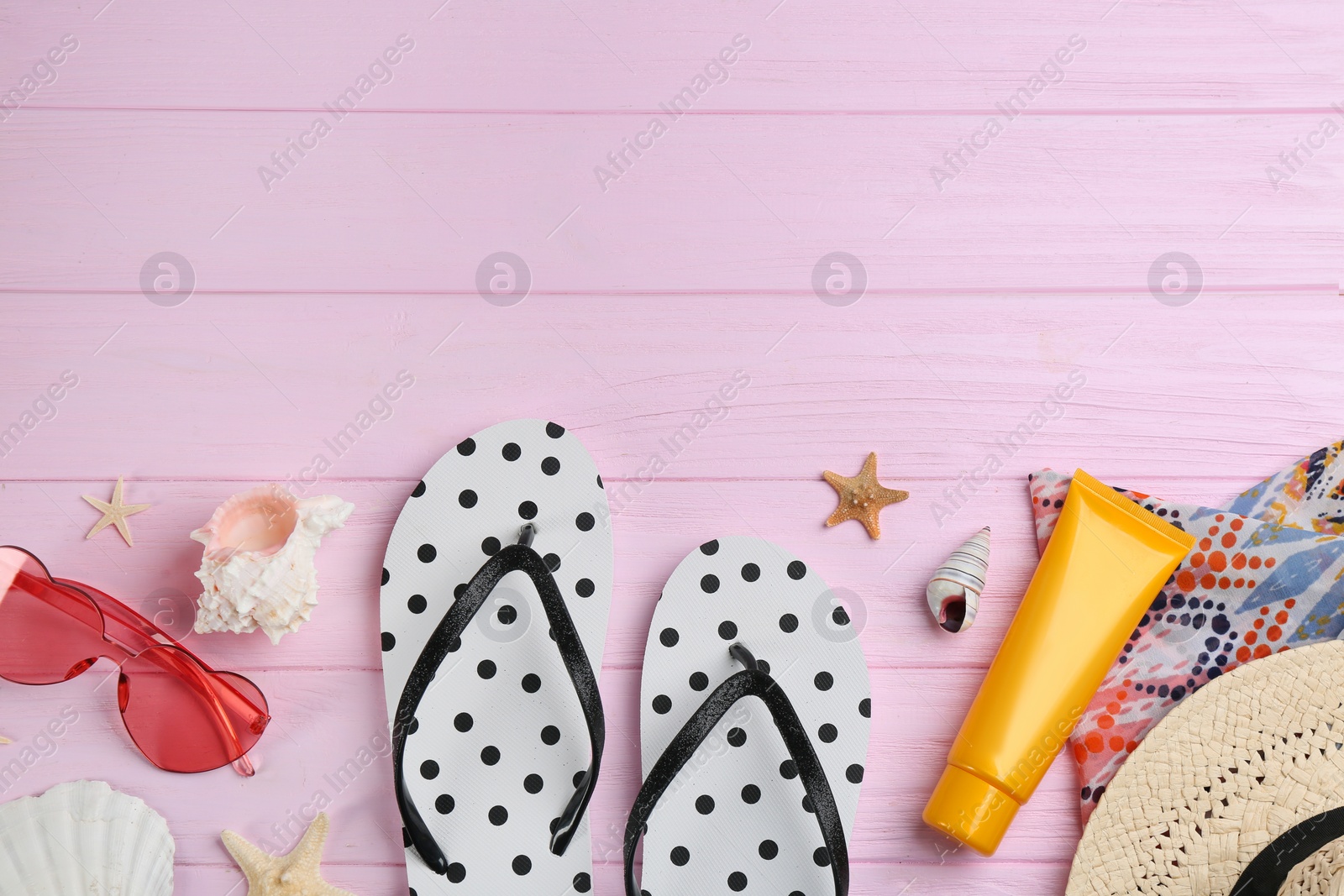 Photo of Flat lay composition with flip flops and beach accessories on pink wooden background. Space for text