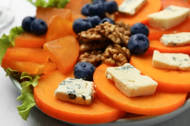 Delicious persimmon with blue cheese, blueberries and walnuts on plate, closeup