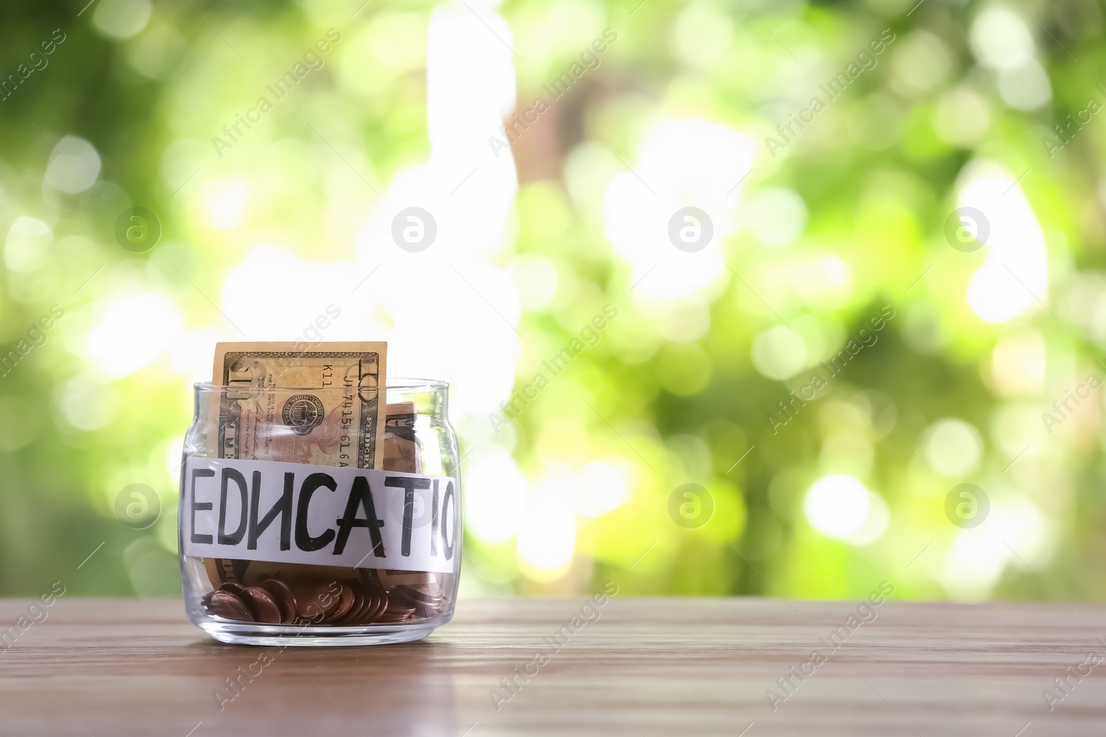 Photo of Glass jar with money and word EDUCATION on table against blurred background, space for text
