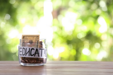Photo of Glass jar with money and word EDUCATION on table against blurred background, space for text