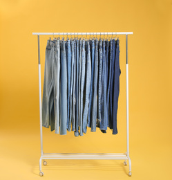 Rack with different jeans on yellow background