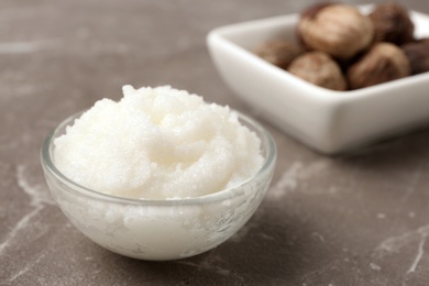 Photo of Shea butter in bowl and nuts on grey background. Space for text