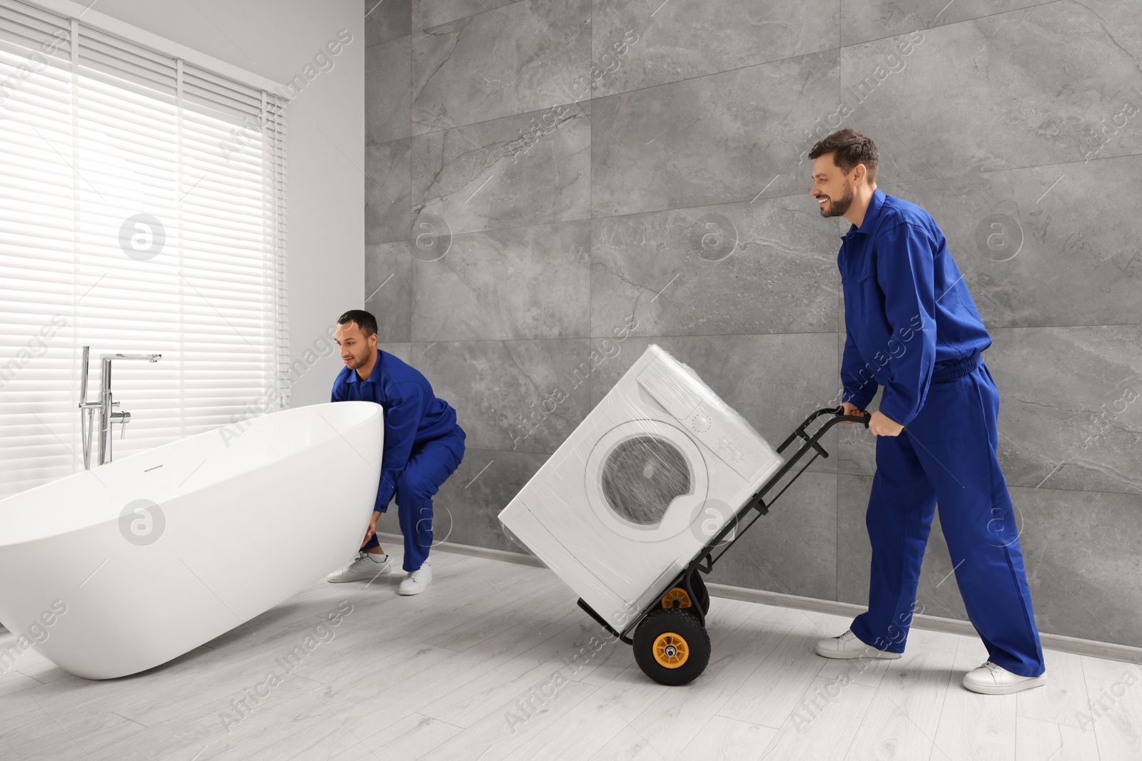 Photo of Male movers with bathtub and washing machine in bathroom. New house